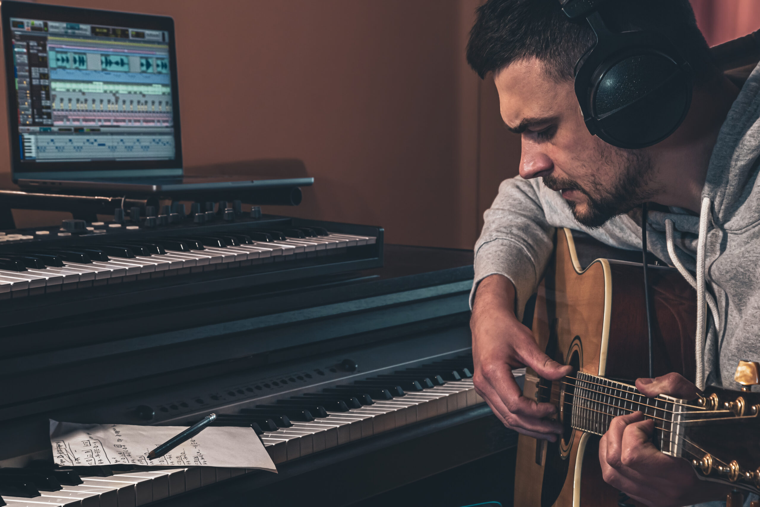 Male musician plays the acoustic guitar at home in the workplace near the computer and piano.